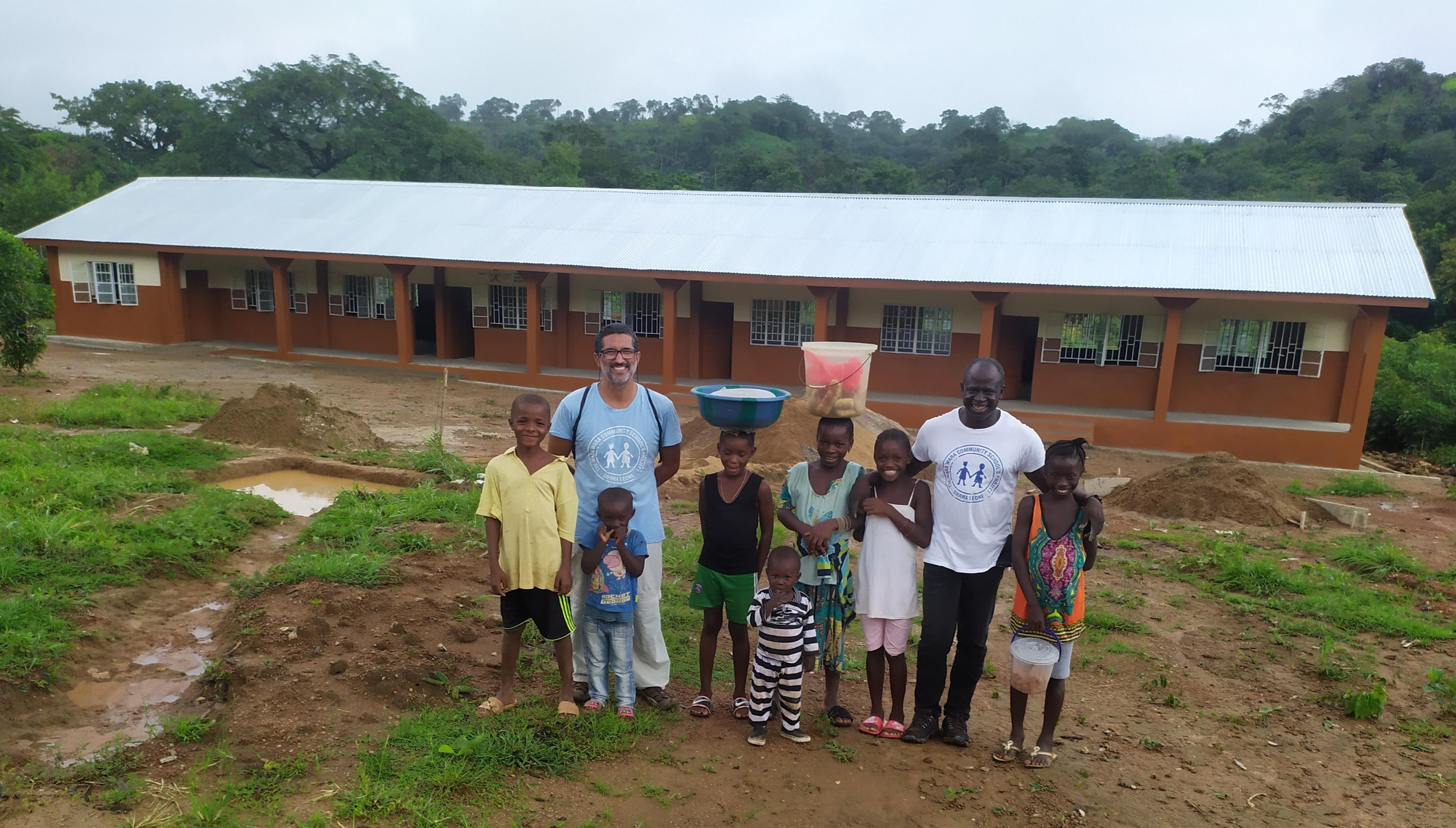 Responsables de las escuelas Wara Wara rodeados de niños con la nueva escuela a la espalda
